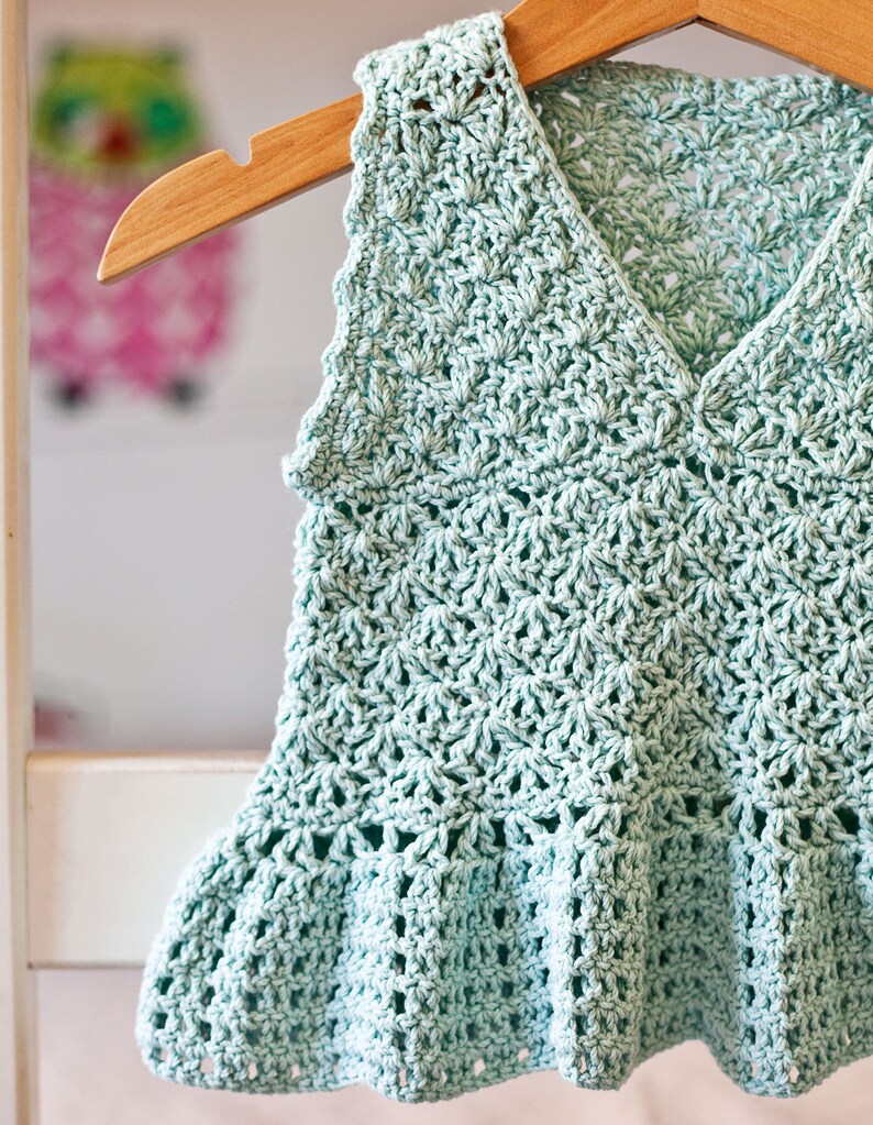 May include: A light blue crocheted sleeveless top with a scalloped hem and a V-neck.