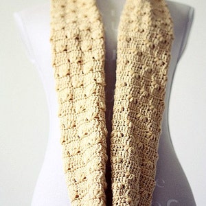 May include: A beige crocheted infinity scarf with a textured pattern.