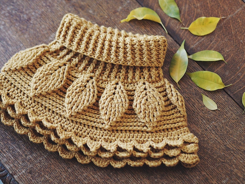 May include: A crocheted cowl with a leaf pattern in a warm brown color. The cowl has a folded over collar and a scalloped edge.