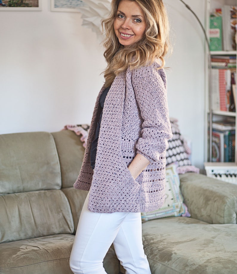 May include: A light purple crocheted cardigan with long sleeves and pockets. The cardigan is open in the front and has a loose fit.