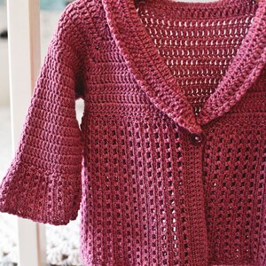 May include: A pink crocheted cardigan with a large collar and a single button closure.