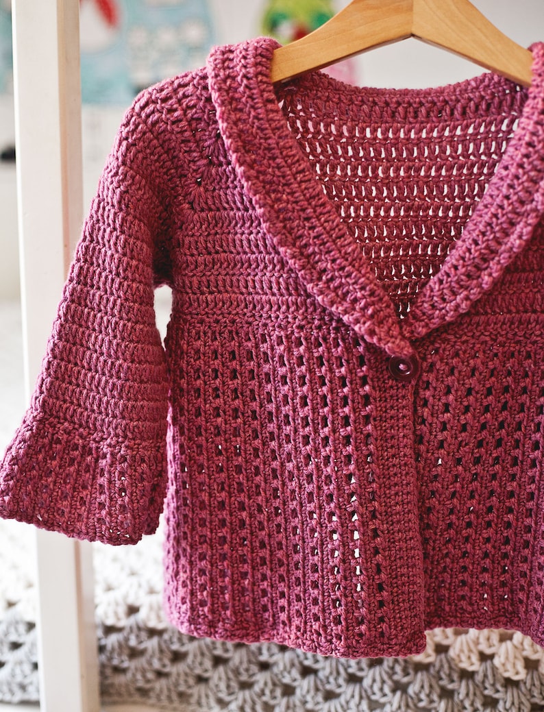 May include: A pink crocheted cardigan with a large collar and a single button closure.