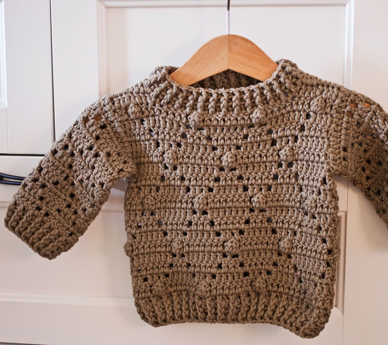 May include: A brown crocheted sweater with a textured pattern. The sweater has a round neckline and long sleeves.