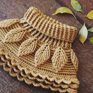 May include: A crocheted garment with a leaf pattern in a mustard yellow color. The garment has a scalloped edge and is made with a textured stitch.