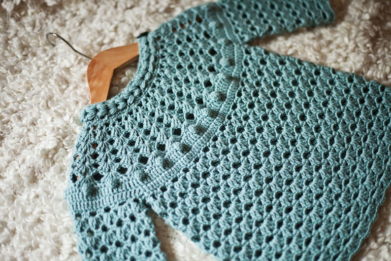 Puede incluir: Un su&eacute;ter de crochet azul claro con un delicado patr&oacute;n de calado. El su&eacute;ter tiene un cuello redondo y mangas largas.