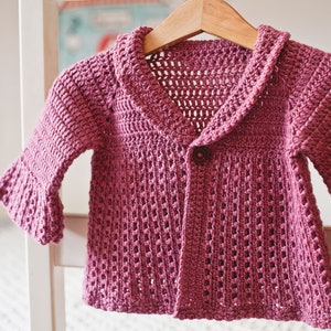 May include: A pink crocheted cardigan with a button closure and a wide collar. The cardigan has a lacy pattern and is made with a soft yarn.