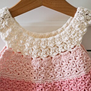 May include: A crocheted baby dress with a white crocheted collar and a pink ombre design.