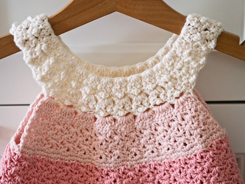 May include: A crocheted baby dress with a white crocheted collar and a pink ombre design.