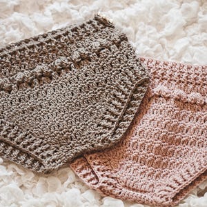 Puede incluir: Dos bragas de ganchillo hechas a mano en colores neutros. Una es marrón claro, la otra rosa suave. Ambas tienen un patrón de puntadas texturizado y bordes decorativos. Las bragas son probablemente para un bebé o un niño pequeño.