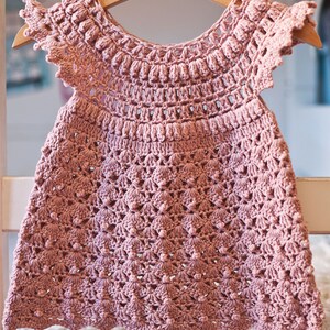 Peut inclure: Une robe de b&eacute;b&eacute; en crochet rose avec un ourlet festonn&eacute; et un motif floral d&eacute;licat.
