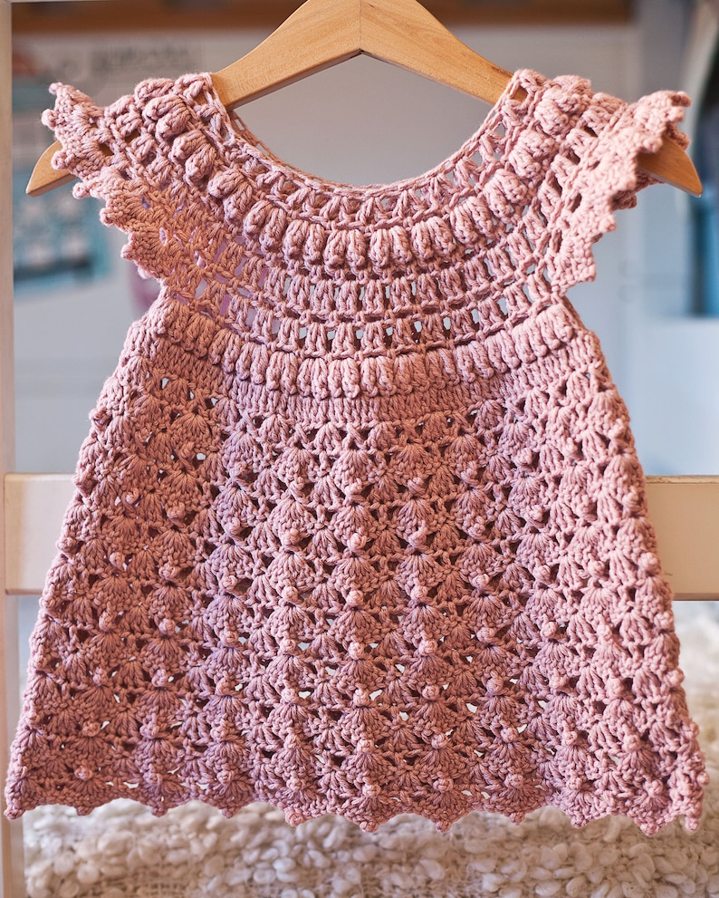 Peut inclure: Une robe de b&eacute;b&eacute; en crochet rose avec un ourlet festonn&eacute; et un motif floral d&eacute;licat.