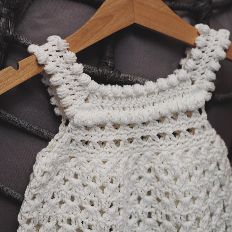 May include: White crocheted top with a delicate, lacy design. The top has a round neckline and a sleeveless design.