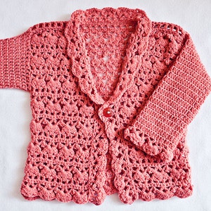 May include: A coral-colored, crocheted cardigan with a scalloped collar and hem. The long-sleeved garment features a single red button closure. The openwork design is visible throughout the sweater, creating a delicate, textured appearance.