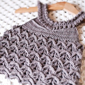 May include: A brown crocheted halter top with a textured pattern. The top is hanging on a wooden hanger.
