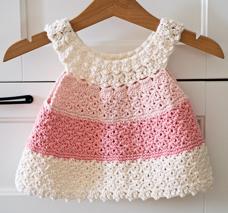 May include: A pink and white crocheted baby dress with a scalloped edge.