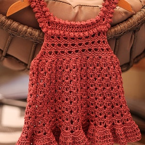 May include: A crocheted baby dress in a deep pink color with a scalloped hem and a delicate lace pattern.