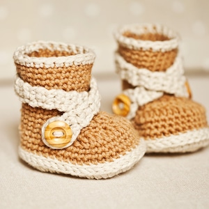 May include: A pair of crocheted baby booties in brown and white with a wooden button accent.