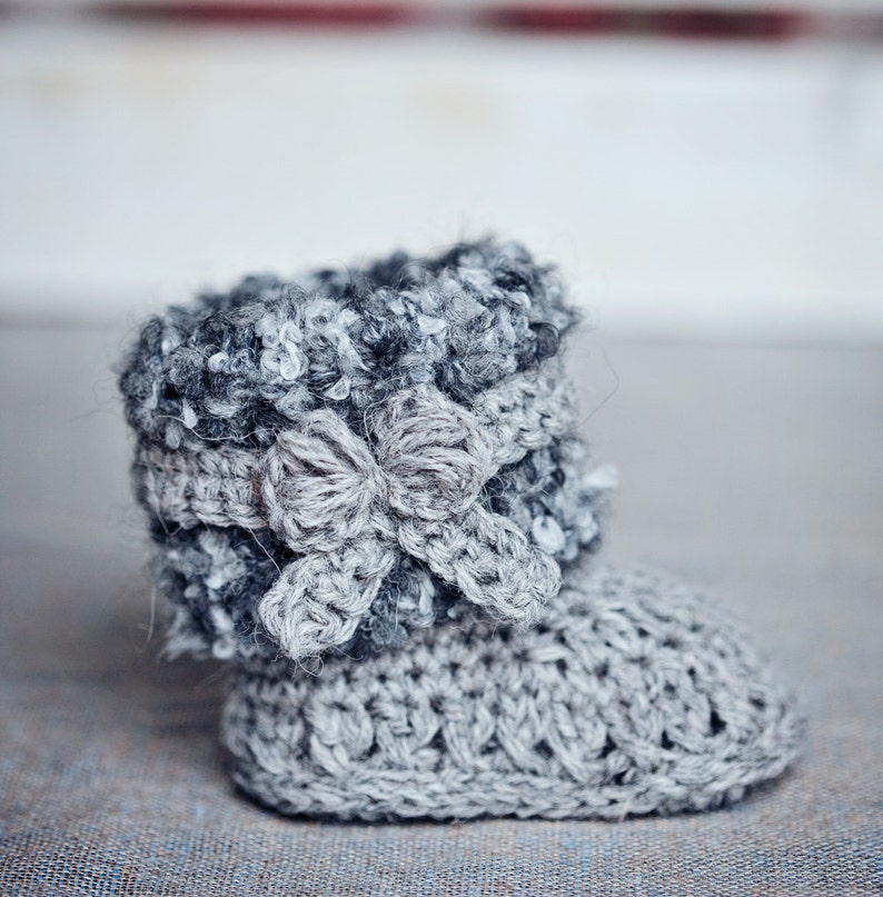 Puede incluir: Botas de beb&eacute; de ganchillo grises con un lazo gris y blanco en la parte superior.