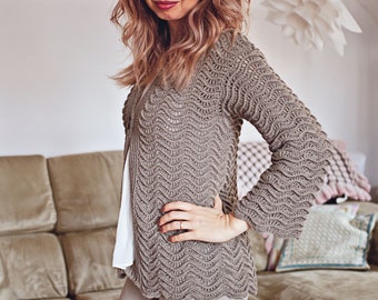 May include: A woman wearing a brown crocheted cardigan with a wavy pattern. The cardigan has long sleeves and a relaxed fit. She is wearing it over a white top and beige pants.