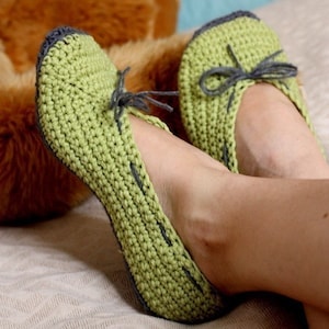 May include: Green knitted slippers with gray trim and a bow. The slippers are made with a simple stitch pattern and have a comfortable, casual look.