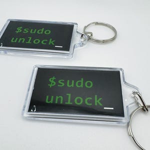 May include: Two clear plastic keychains with black backgrounds and green text that reads "$sudo unlock_"