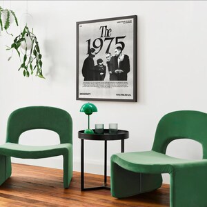 May include: Two green velvet chairs with a black side table and a green lamp in front of a black framed poster with the text "The 1975" in white.