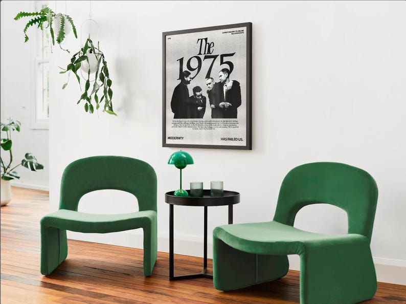 May include: Two green velvet chairs with a black side table and a green lamp in front of a black framed poster with the text "The 1975" in white.