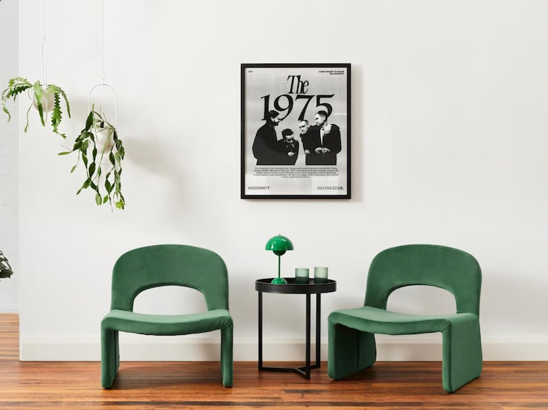 May include: Two green velvet chairs with a black side table and a green lamp in between. A black and white poster of the band "The 1975" hangs on the wall behind the table.