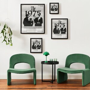 May include: Four black framed posters with the text "The 1975" in white. The posters are hanging on a white wall. Two green velvet chairs and a black side table with a green lamp are in front of the wall.