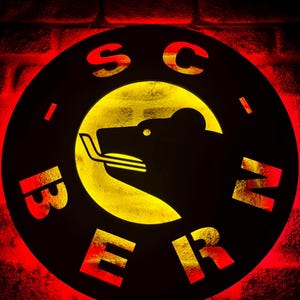 以下が含まれることがあります： 縁に「SC BERN」という文字が書かれた黒と黄色の円形看板。看板の中央には、黄色の背景に黒い熊のシルエットが描かれている。
