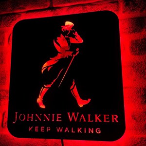 May include: A black metal sign with a red glow behind it. The sign features a silhouette of a man walking with a cane and the text "JOHNNIE WALKER KEEP WALKING".