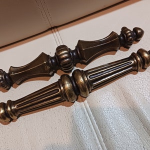 May include: Two antique brass door handles with ornate designs. The handles are in a vintage style and have a worn finish.