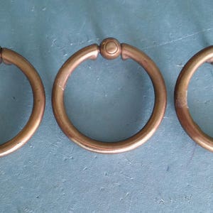 May include: Three antique brass ring pulls with a smooth, rounded finish. The rings are all the same size and shape, and they have a simple, elegant design.