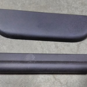 May include: Two black plastic car door handles. The top handle is curved and the bottom handle is straight.