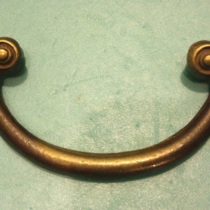 May include: A brass cabinet pull with a curved shape and decorative scrollwork on the ends.