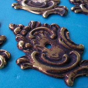 May include: Four ornate, gold-toned metal decorative accents with intricate floral designs. The accents have a worn, antique look and are perfect for adding a touch of vintage charm to home decor projects.