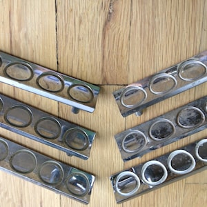 May include: Six chrome-plated metal drawer pulls with rounded edges and four circular cutouts. The pulls are arranged in two rows of three.