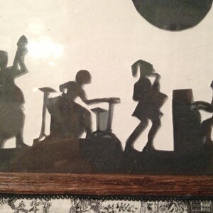 May include: Black silhouette artwork of a band playing music. The band consists of four figures: a drummer, a guitarist, a saxophonist, and a pianist. The artwork is framed and displayed on a wall.