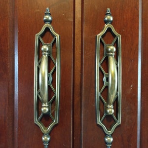 May include: Two ornate brass cabinet door pulls with a geometric design and a rounded handle.