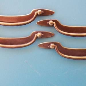 May include: Four antique brass cabinet pulls with a curved design. The pulls have a smooth, polished finish.