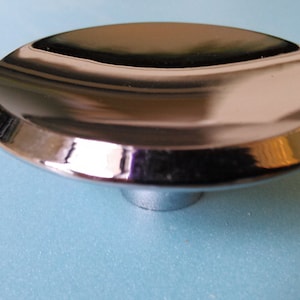 May include: A shiny, silver, round, decorative cabinet knob with a raised, circular base.