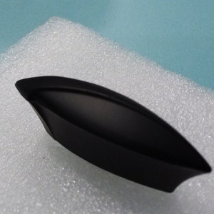 May include: Black cabinet pull with a curved, slightly rounded shape. The pull is made of metal and has a matte finish.