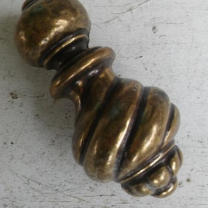 May include: Close-up of a vintage brass furniture knob. The knob has a detailed, spiral design on the handle and a rounded top. The brass has a warm, aged patina, suggesting it's an antique or vintage piece.