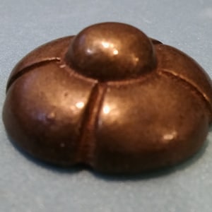 May include: A small, bronze-colored, decorative object shaped like a flower with four petals and a rounded center.