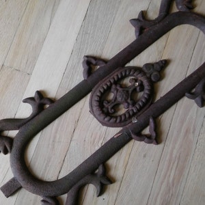 May include: A rusty metal decorative piece with a floral design and an oval shape. The piece has a rustic look and is made of cast iron.