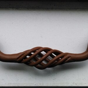May include: A brown metal cabinet door pull with a twisted design. The pull has two round knobs on each end.