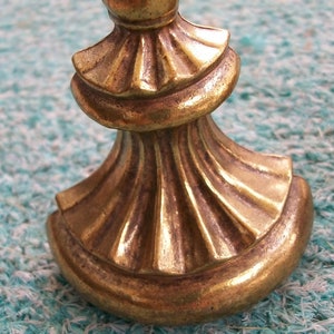 May include: A gold-toned metal finial with a decorative, fluted design. The finial has a rounded top and a base that is shaped like a half-circle.