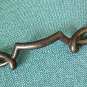 May include: A brass cabinet pull with a unique, abstract design. The pull has a curved shape with a loop at each end.