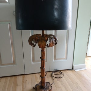 May include: A gold palm tree-shaped floor lamp with a black lampshade. The lamp has a rustic, vintage look.