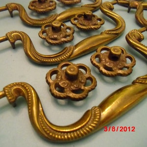 May include: Set of six antique brass cabinet knobs with ornate floral designs. Each knob features a decorative, swirling handle and a round, fluted base.